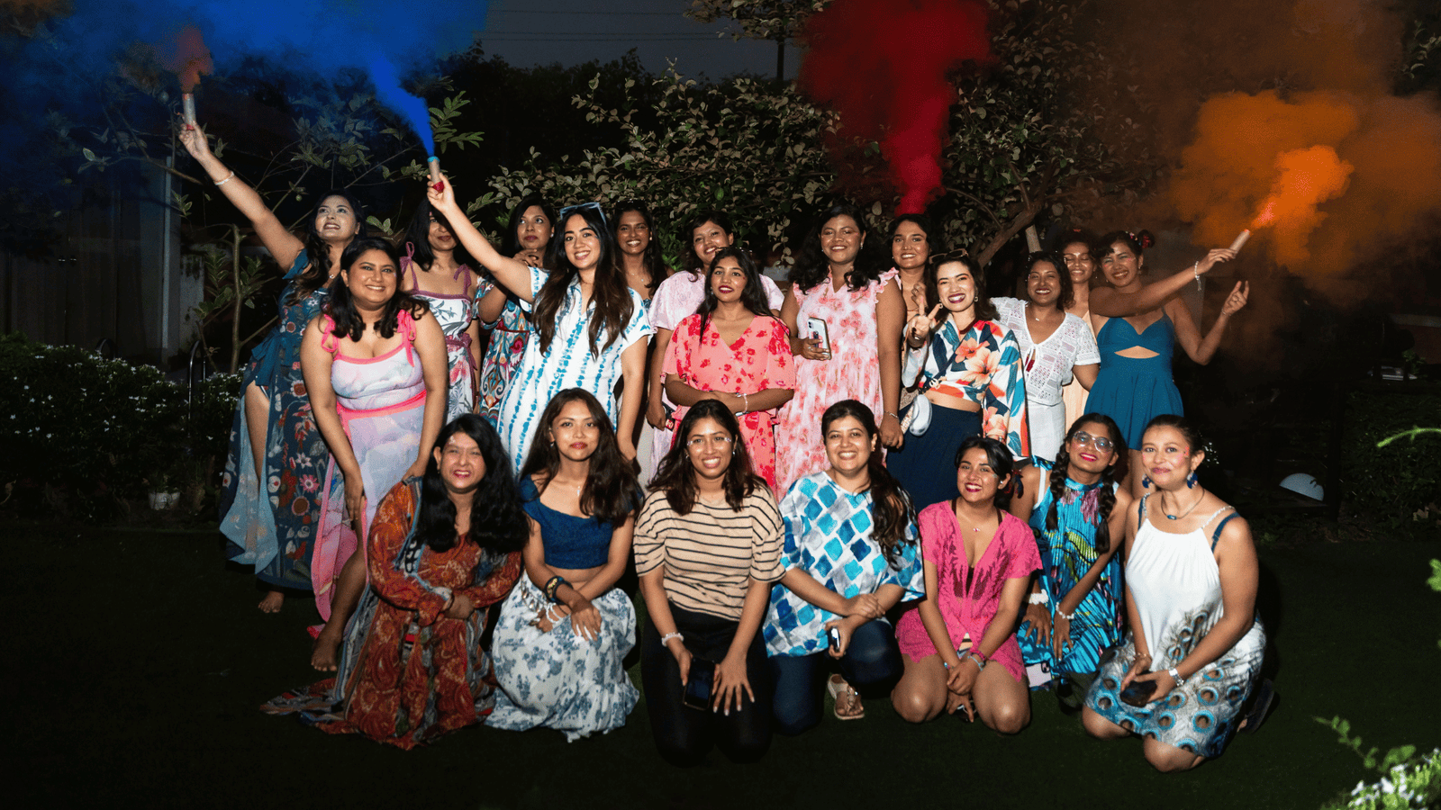 The SHAPE Lingerie team and friends standing together on a lawn at night, holding coloured smoke flares